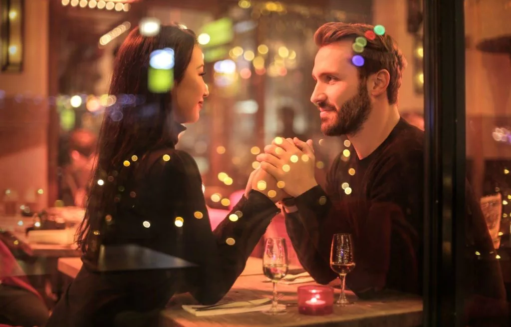 A man and a woman sitting in a restaurant across from each other clasping each other
