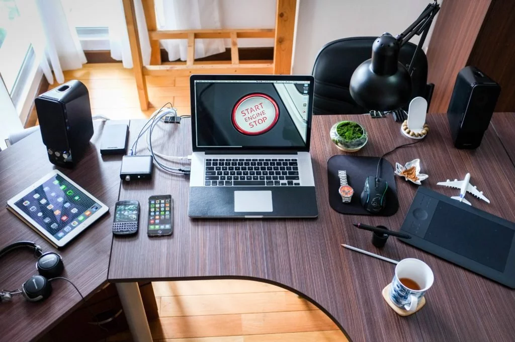 Desk with multiple phones, computer earphones, coffee cup, speaks and an Ipad in an office