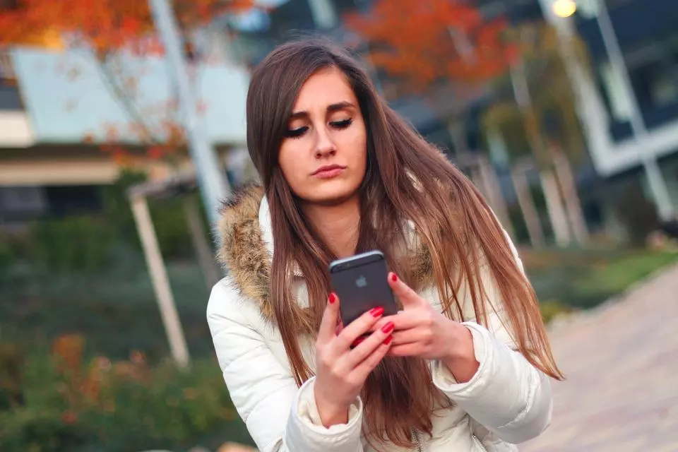 girl outside wearing a white jacket checking her phone 