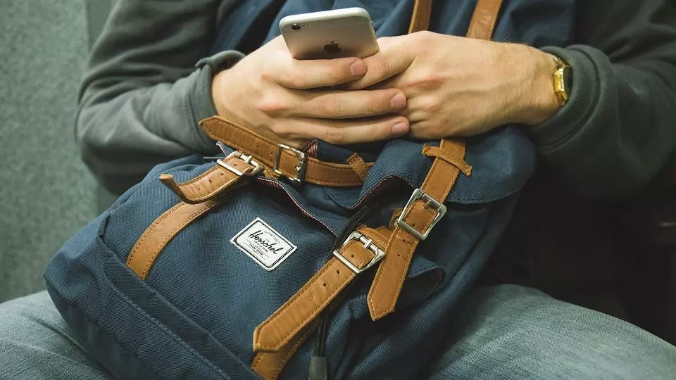 Man holding cell phone, hands are resting on a backpack