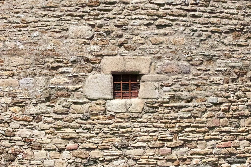 stone wall with tiny window that has bars in it