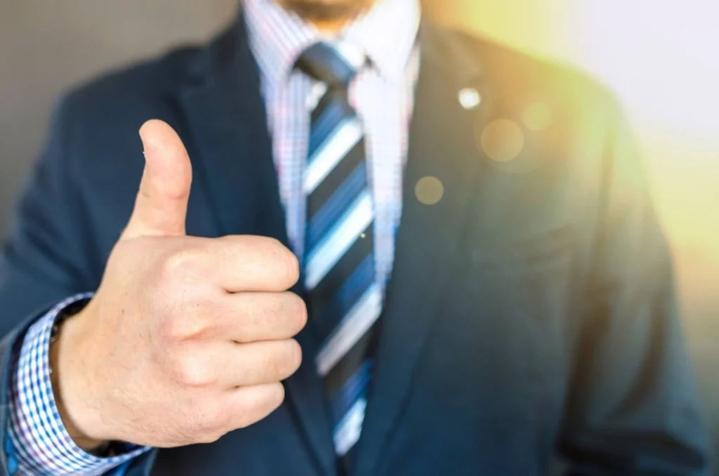 A man in a suit giving a thumbs to a business deal done