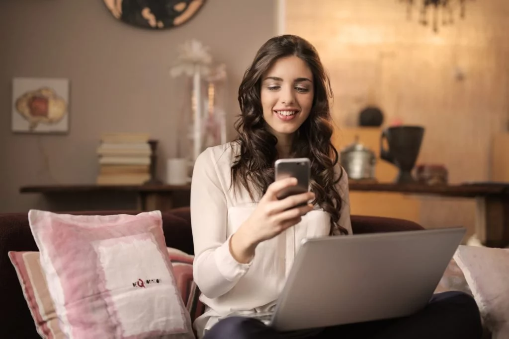 woman-using-cellphone-smartphone-and-laptop-in-apartment