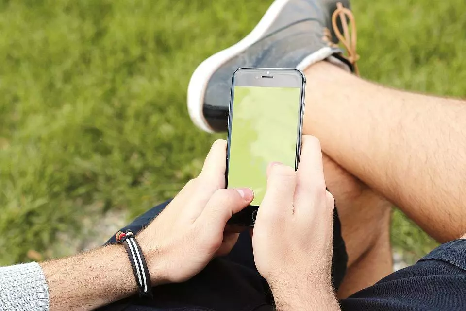 Stock image of person holding phone, with grass in background