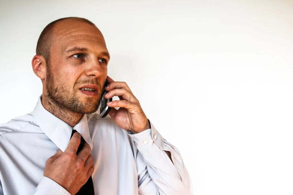 Man with an uncomfortable look on his face , on the phone , nervously fussing with his tie