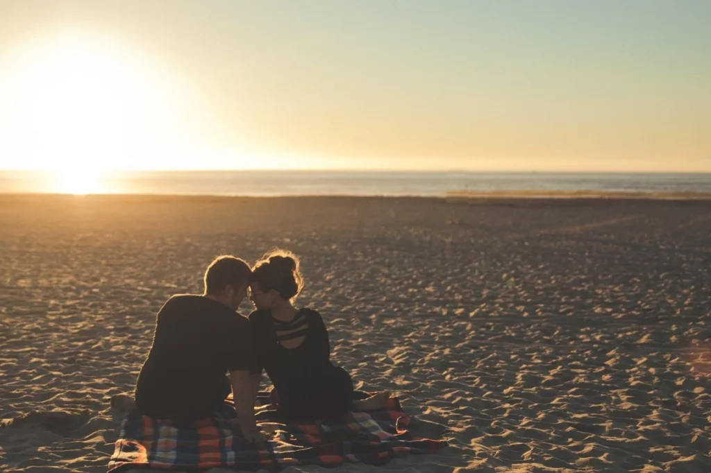 A couple sitting by the beach on a blanket at sunset about to kiss