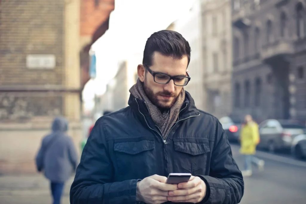 man with a beard standing on the street looking at his phone