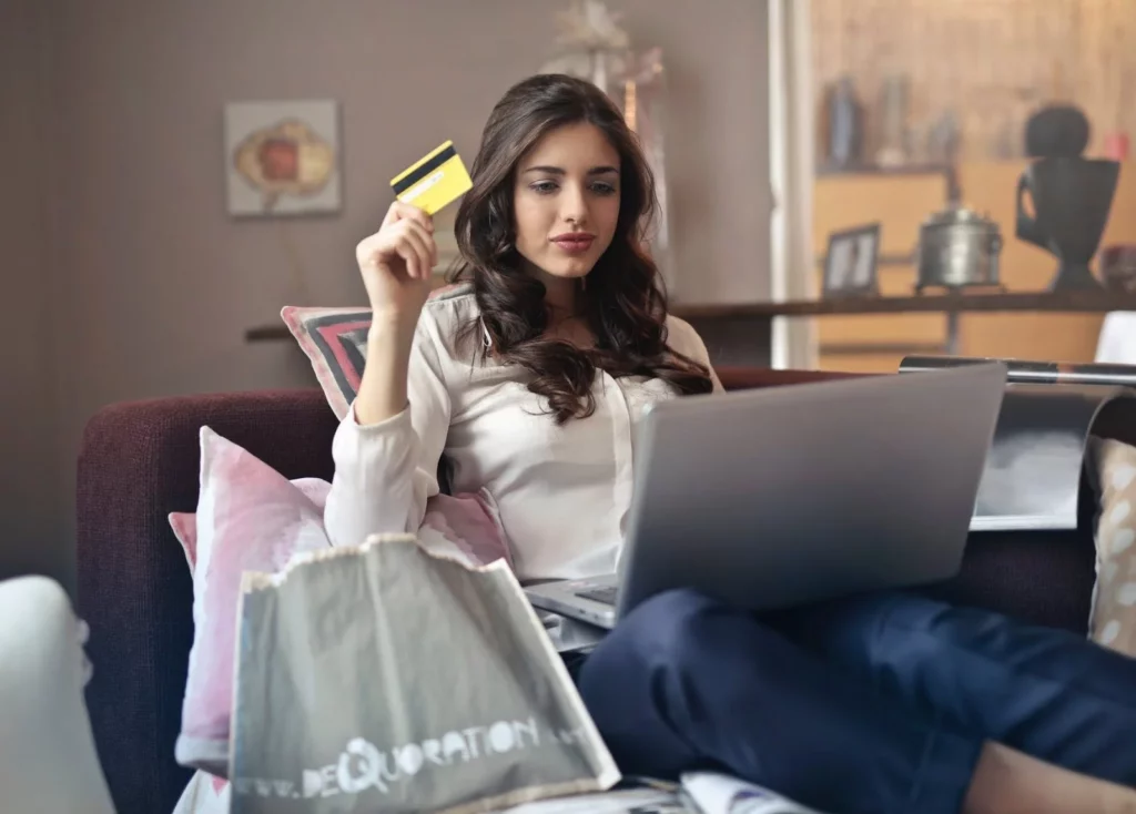 Girl with brown hair sitting at her computer holding a credit card about to buy something